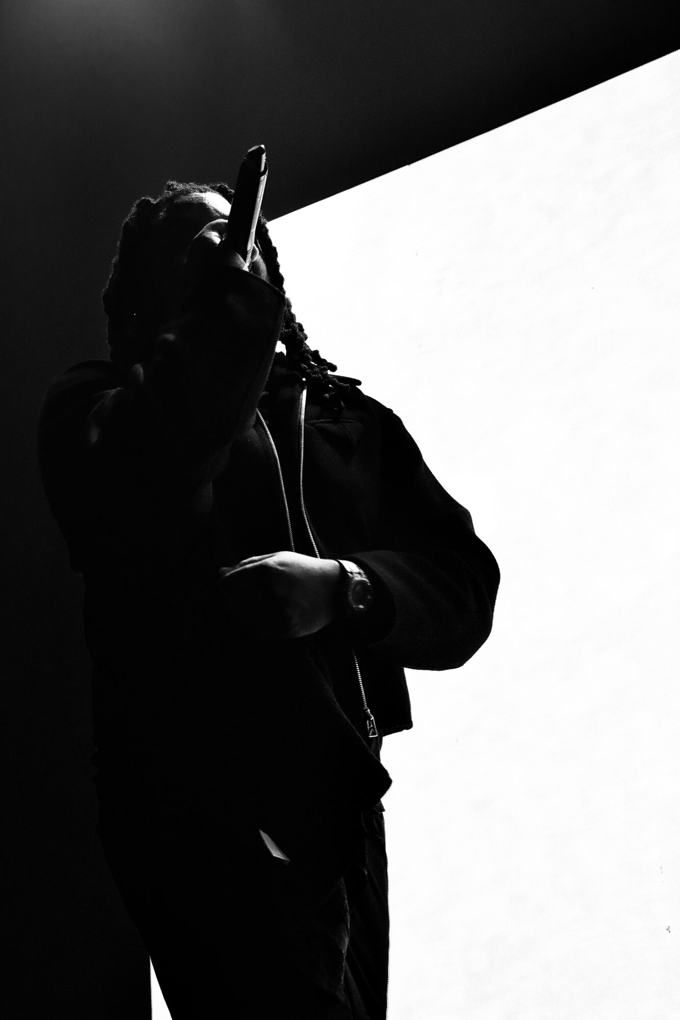 Silhouette of a person holding a microphone, standing against a bright background, with a dark upper background.