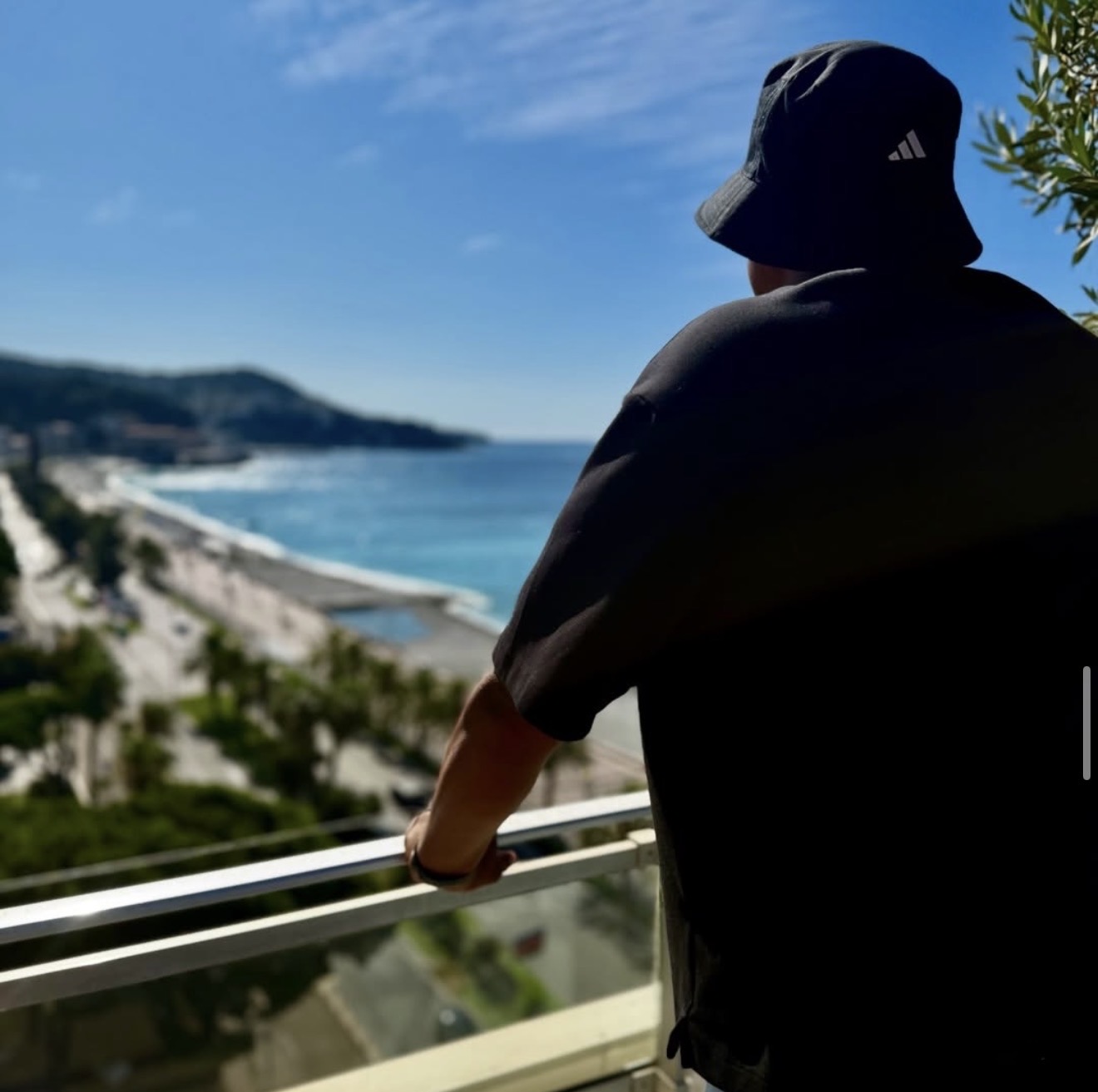 Person wearing a bucket hat looking at a coastal view from a balcony, with ocean and sky in the background.