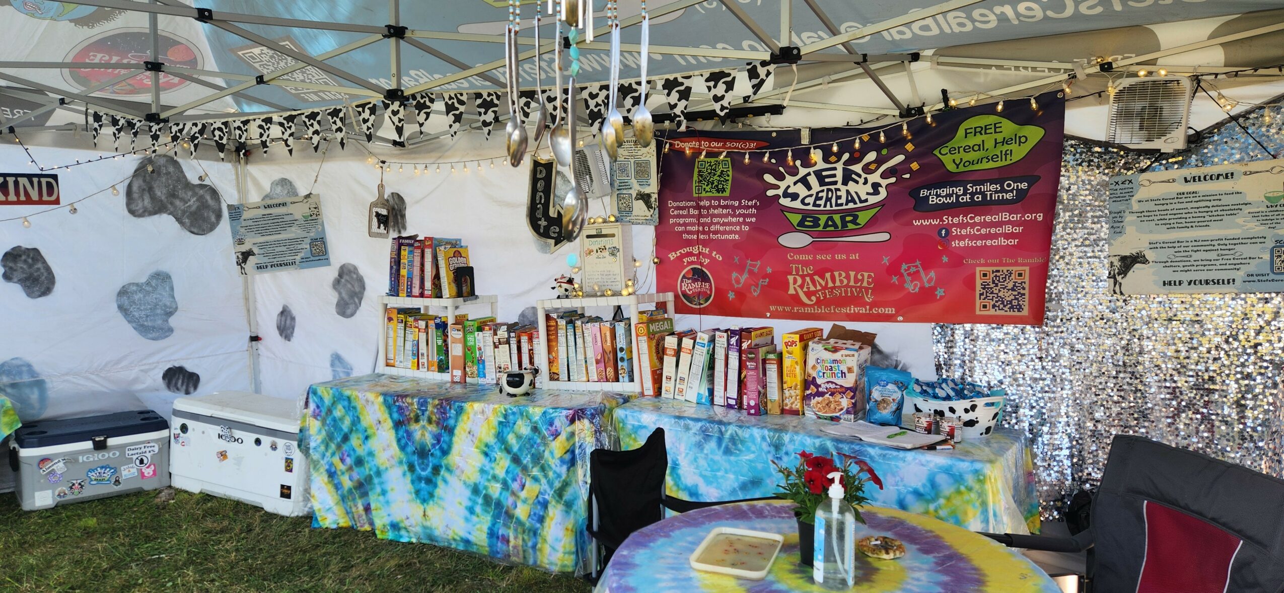Bookshelves with books, a table with a tablecloth, and decorations inside a tent at an outdoor event.