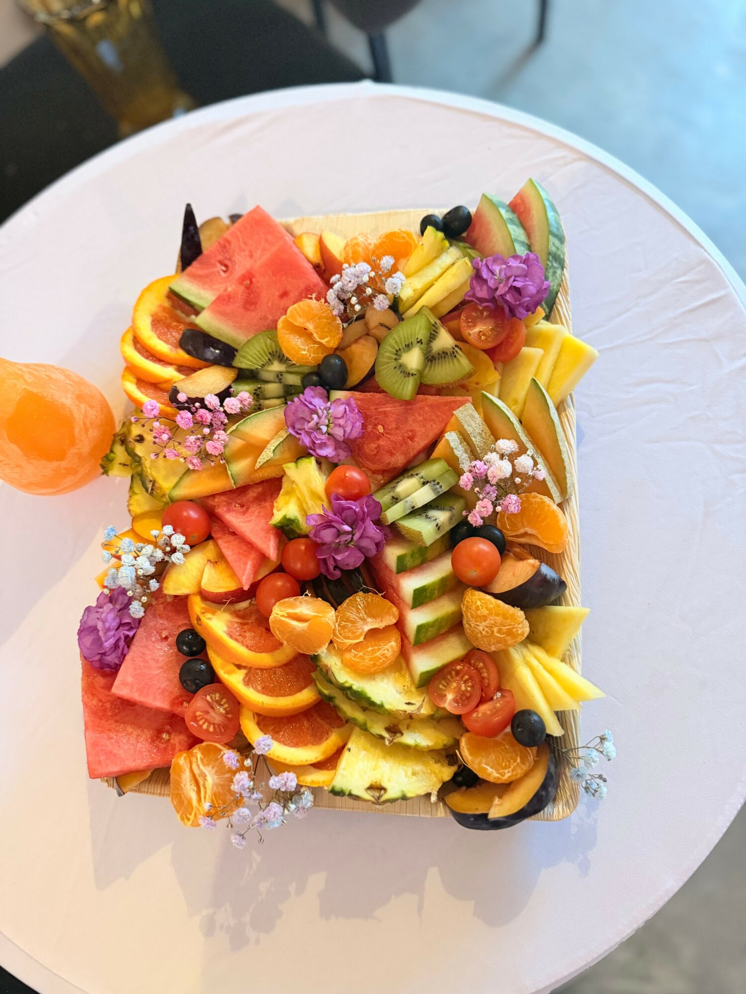 Plate with colorful fruit and flower garnishes, including watermelon, kiwi, mango, and edible purple flowers, on a white dish.