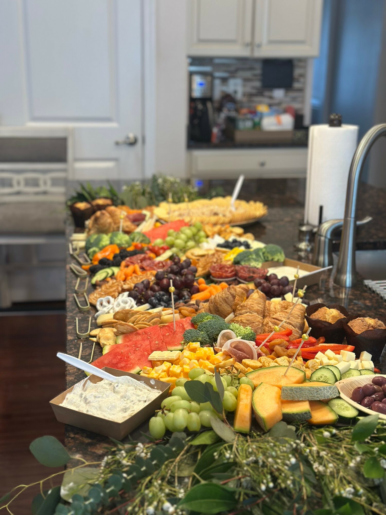 A long table with various colorful foods, including fruits, vegetables, and snacks, in a kitchen setting.