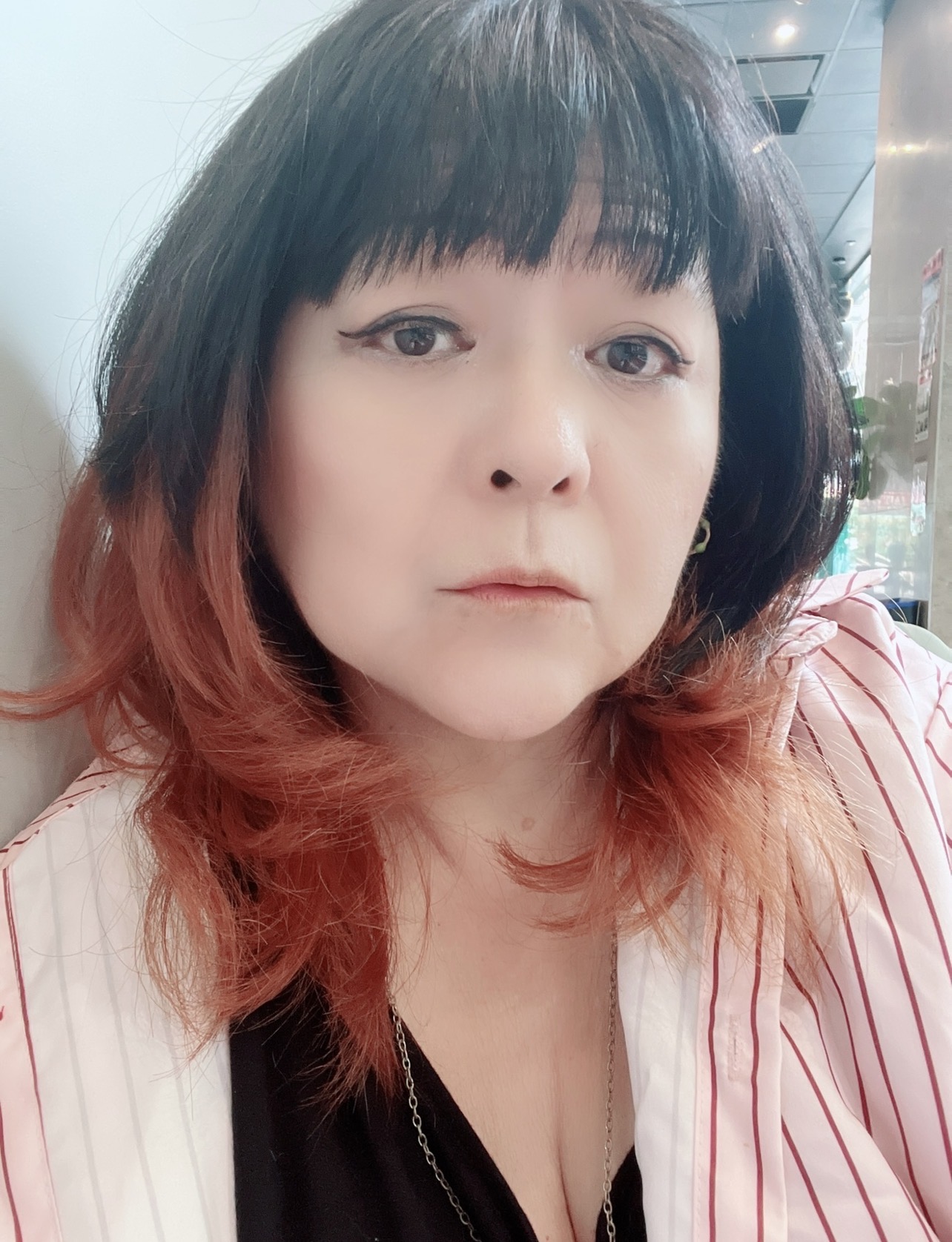 Woman with black and red hair, wearing a striped shirt, looking at the camera indoors.