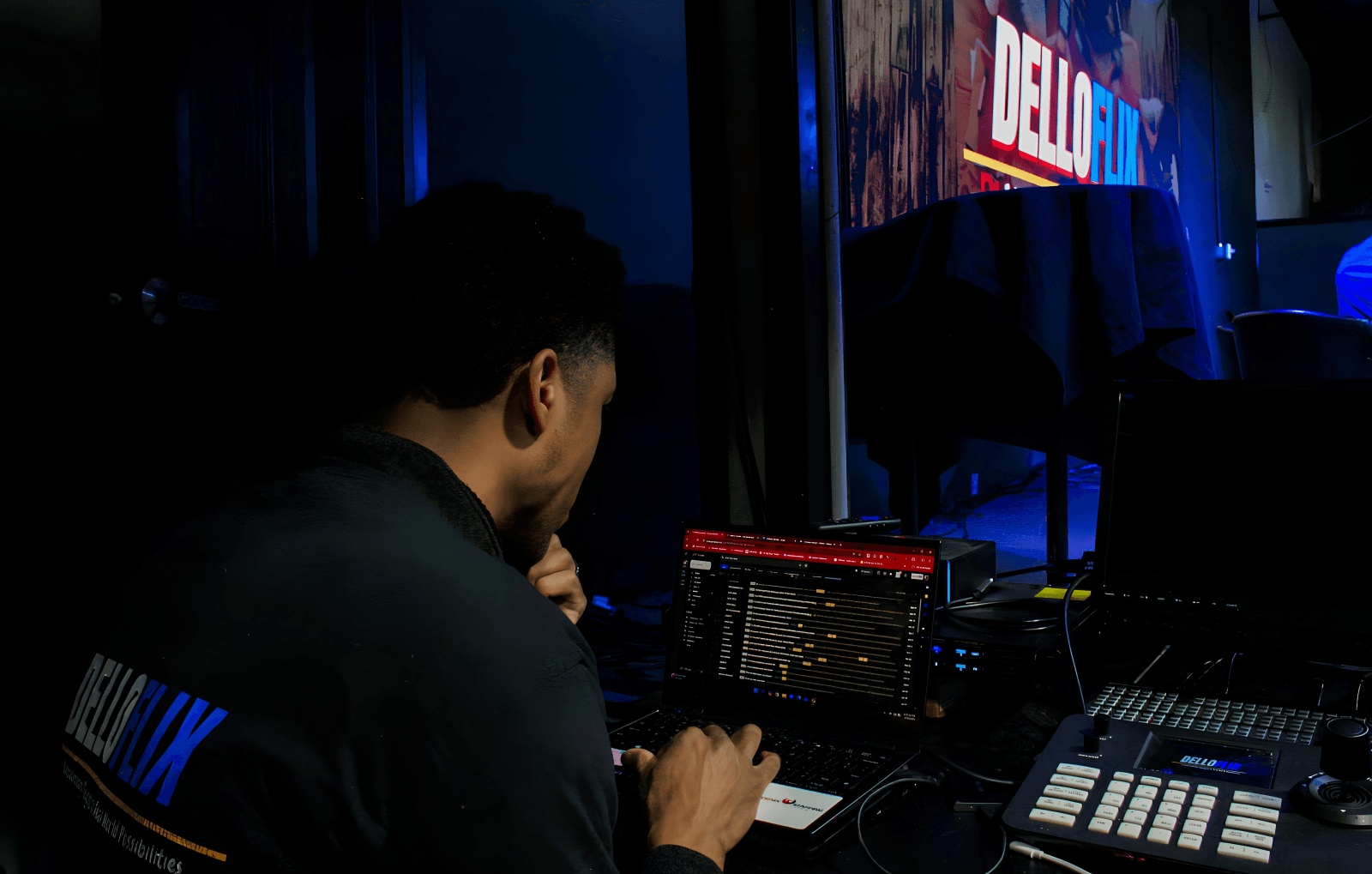Person working with audio equipment in a dark room, illuminated by screens and equipment lights.