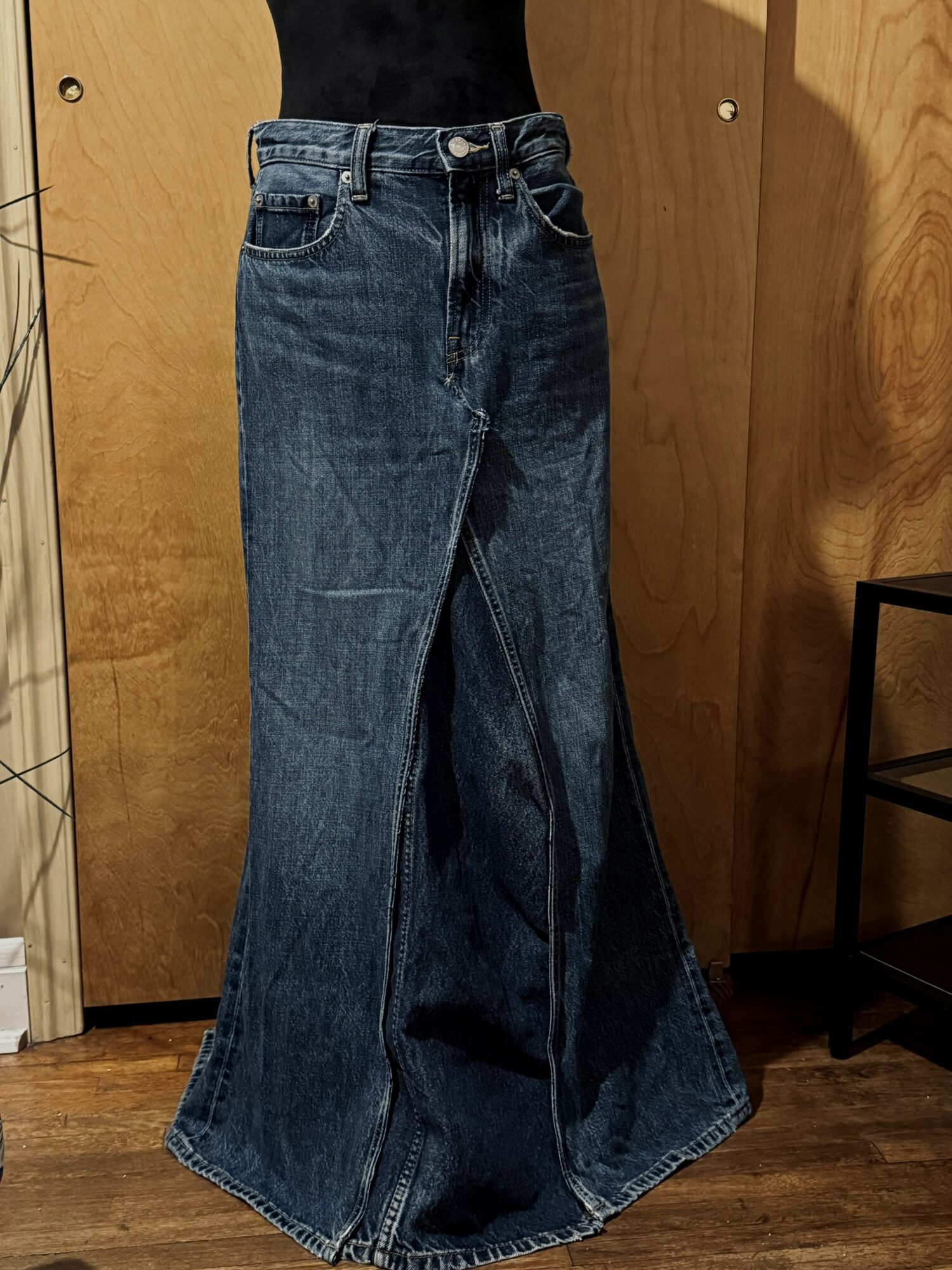 Person wearing high-waisted wide-leg jeans, black top, standing indoors with wooden door and furniture nearby.
