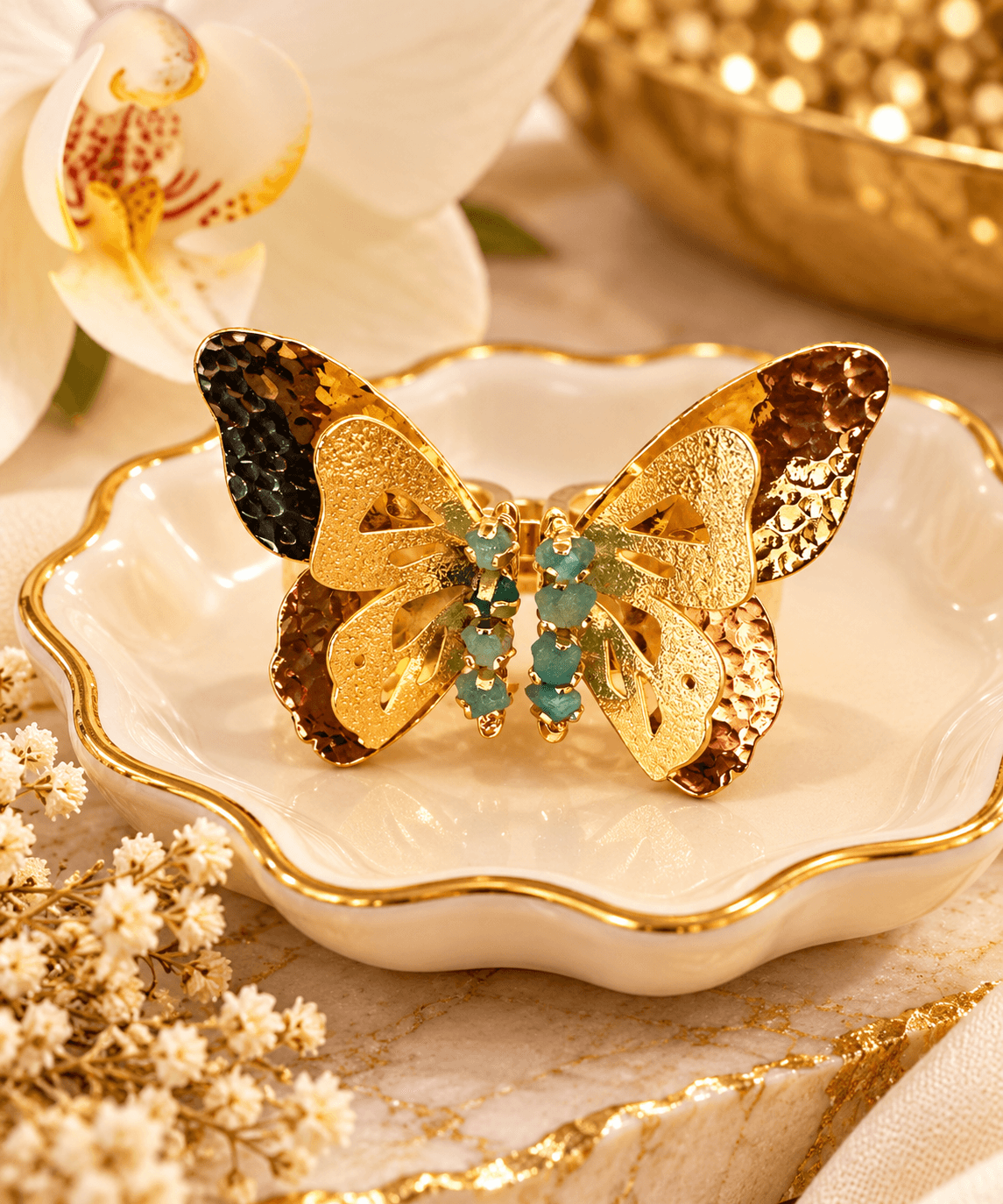 Decorative butterfly ornament with gold, black, and turquoise details on a white dish with gold trim, surrounded by flowers and a gold bowl.