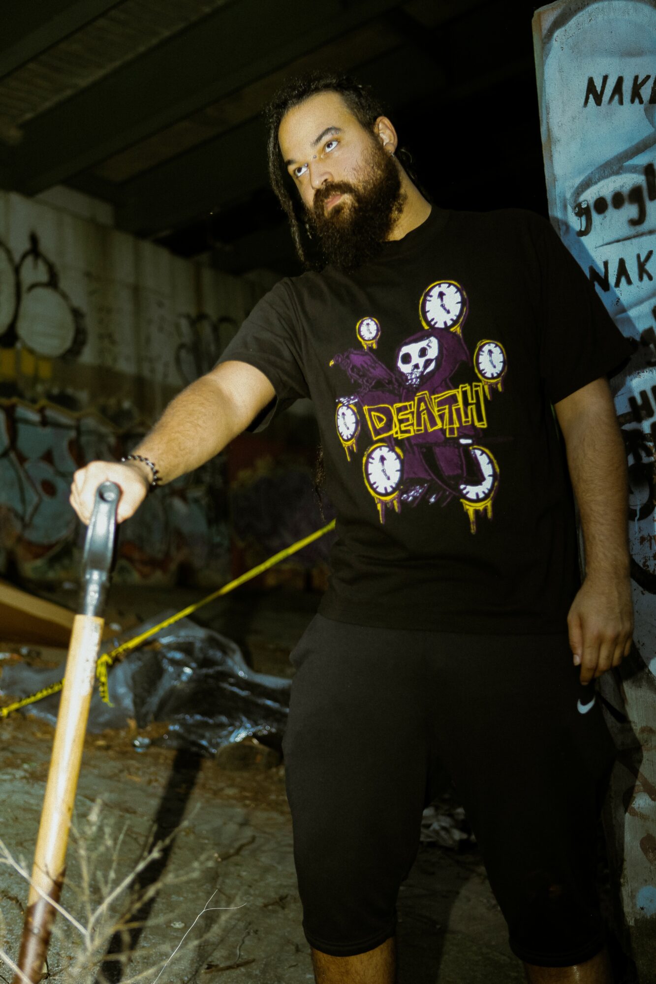Man with a beard and long hair, wearing a black T-shirt with colorful graphics, standing outdoors at night.